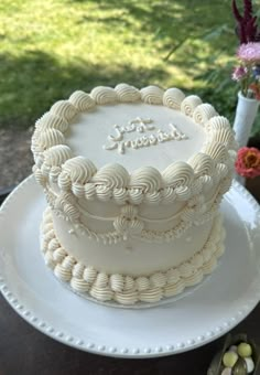 a white frosted cake sitting on top of a table next to a flower vase