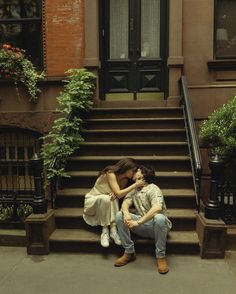 two people sitting on the steps of a brownstone building with their faces close to each other