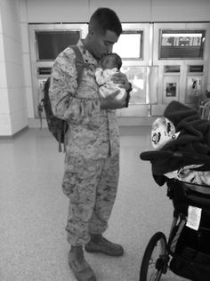 a man in uniform holding a baby next to a stroller