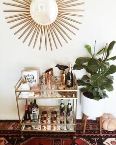 a gold bar cart with bottles on it in front of a wall mounted sunburst