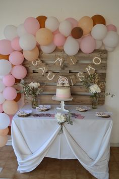 a table topped with a cake and lots of balloons in front of a wooden wall