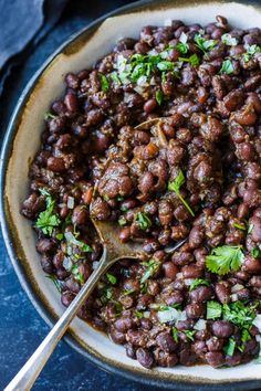 a bowl filled with beans and parsley on top of a blue tablecloth next to a spoon