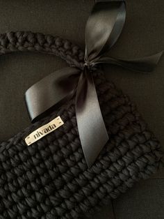 there is a black knitted bag with a ribbon on the handle and tag attached to it