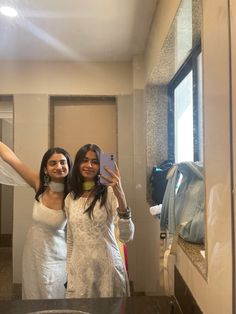 two women taking a selfie in a bathroom mirror