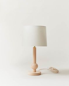 a wooden table lamp with a white shade on the base and a cord plugged into it