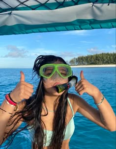 a woman wearing goggles and giving the thumbs up sign while standing on a boat