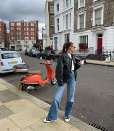 a woman standing on the side of a road next to parked scooters and cars