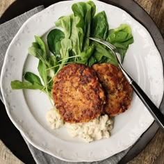 two crab cakes on a white plate with spinach leaves and a fork next to it