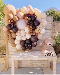 a teddy bear sitting on a bench next to a bunch of balloons