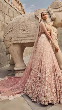 a woman standing next to an elephant statue wearing a pink gown and headpieces