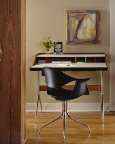 an office with a desk, chair and painting on the wall behind it in a home