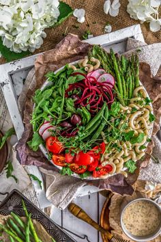 a bowl filled with noodles and vegetables on top of a wooden table next to flowers