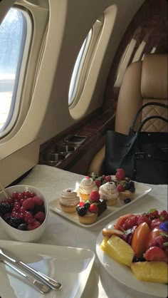 desserts are served on plates in front of an airplane's windows as well as fruit and ice cream