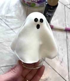 a hand holding a jar with a fake ghost in it's mouth and two other items behind it