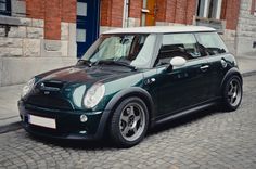 a small green and black car parked on the side of a street next to a brick building