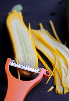 an orange handled vegetable slicer next to yellow and green vegetables on a black surface