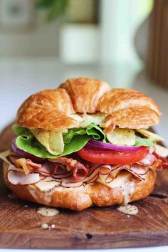 a croissant sandwich with meat, lettuce and tomato slices on it