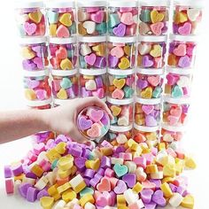 a person holding a container full of candy hearts next to several containers filled with heart shaped candies