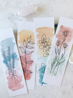 three watercolor cards with flowers on them sitting on a table next to some scissors