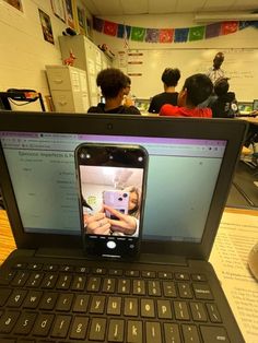 an open laptop computer sitting on top of a wooden table in front of children working at desks