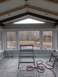 a ladder is in the middle of an empty room with large windows on both sides