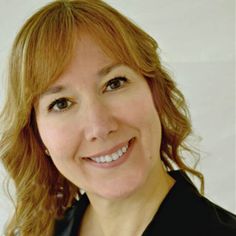 a woman with red hair smiling at the camera and wearing a black jacket over her shoulders