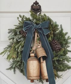 a wreath with two bells hanging from it's side and pine cones on top