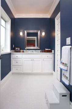 a bathroom with blue walls, white cabinets and a large mirror on the wall above it