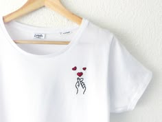 a white t - shirt with red hearts on it hanging from a wooden hanger