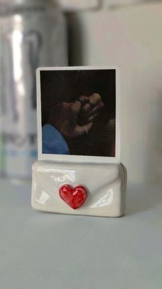 a photo frame with a red heart on it sitting on a counter next to a cup