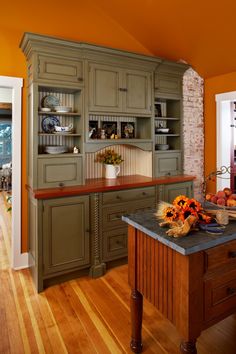 a kitchen with green cabinets and wooden floors, an island in front of the sink