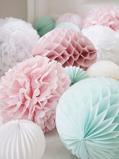 many different colored paper flowers on a white tablecloth with pink, blue and green tissue pom - poms