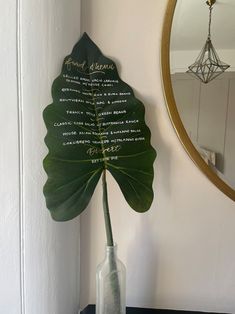 a large green leaf in a vase next to a mirror on a table with writing on it