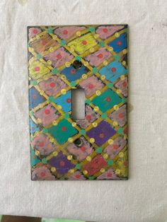 a decorative light switch plate cover in multicolored squares and dots on white paper