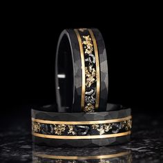 two black and gold wedding bands with floral designs on each side, sitting on a marble surface