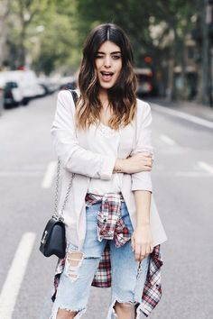 a woman standing on the street with her arms crossed in front of her chest and wearing ripped jeans