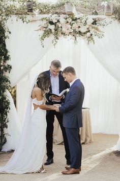 a bride and groom are exchanging vows under an arch decorated with greenery at their wedding