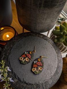 two earrings sitting on top of a rock next to a vase and potted plant