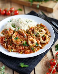 a white plate topped with pasta and meat covered in sauce next to rice on top of a wooden table