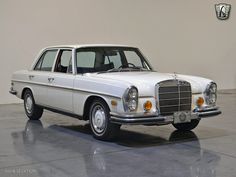 an old white mercedes benz is parked in a room with a black and white logo on the wall