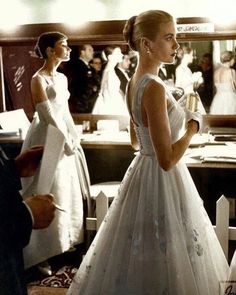 two women in formal dresses standing next to each other and looking at something on the table