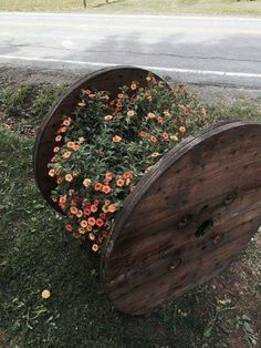 an old wooden barrel with flowers growing out of it on the side of the road