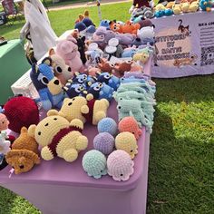 there are many stuffed animals on the table at this outdoor event, including teddy bears