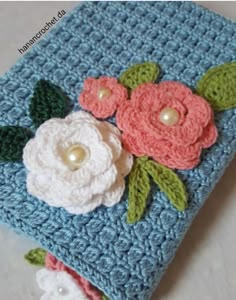 a crocheted book with flowers and pearls on the cover is sitting on a table