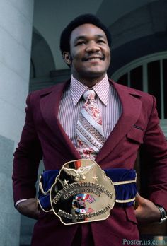 a man in a red suit and tie holding a gold medal with words on it