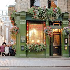 people are standing outside of a store with flowers on the front and side windows,