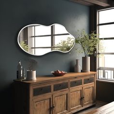 an oval shaped mirror hangs on the wall above a wooden dresser with vases and fruit