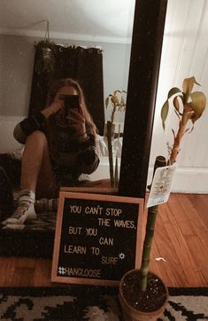 a woman taking a selfie with her cell phone in front of a mirror that says you can't stop the waves but you do it can learn to surf