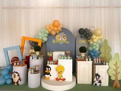 an assortment of balloons and decorations on a table in front of a backdrop with cartoon characters