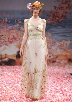 a woman is walking down the runway wearing a dress with flowers on it's head